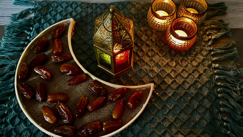A half moon shaped tray with dates and an oriental lamp with three little tea light holder on a green mat for Ramadan decoration
